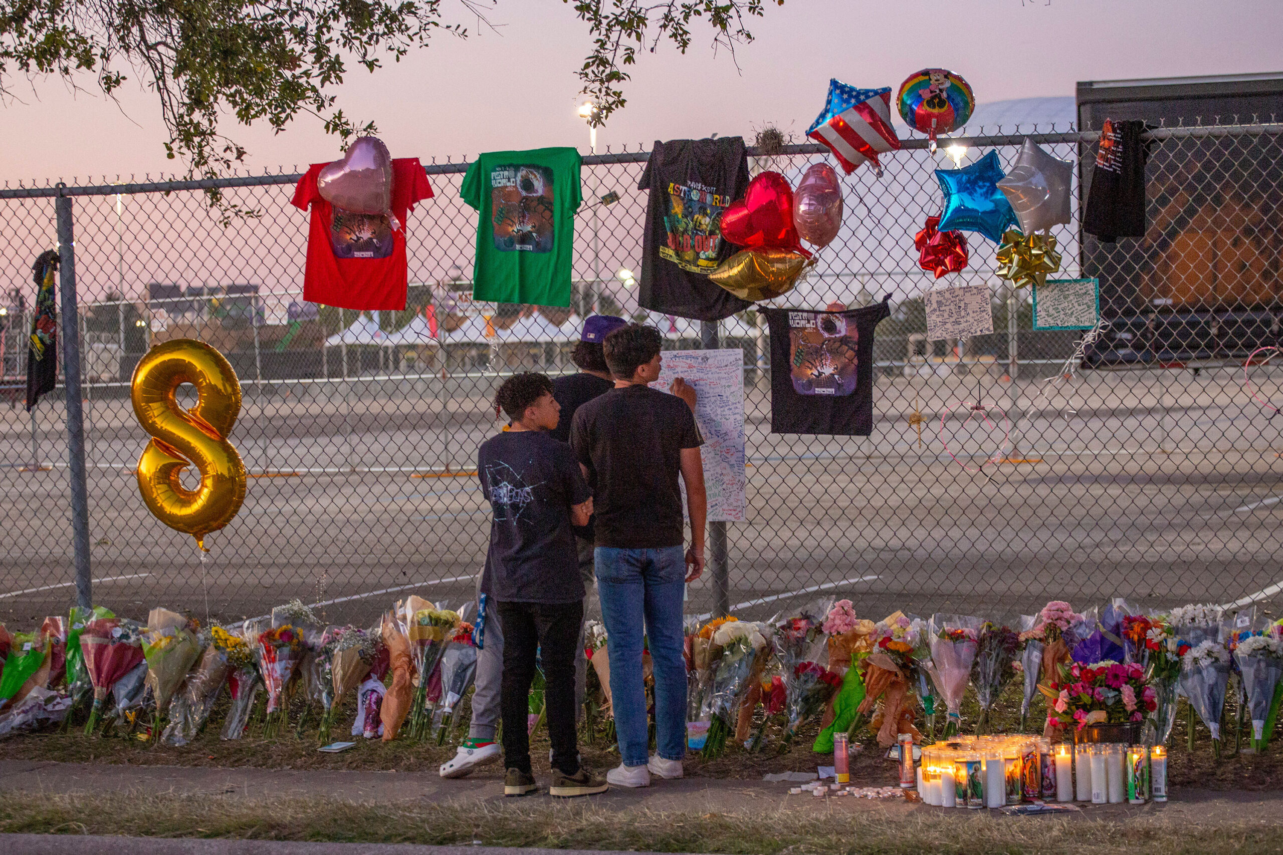 Concert attendees Isaac Hernandez and Matthias Coronel watch Jesus Martinez sign a remembrance board at a makeshift memorial on November 7