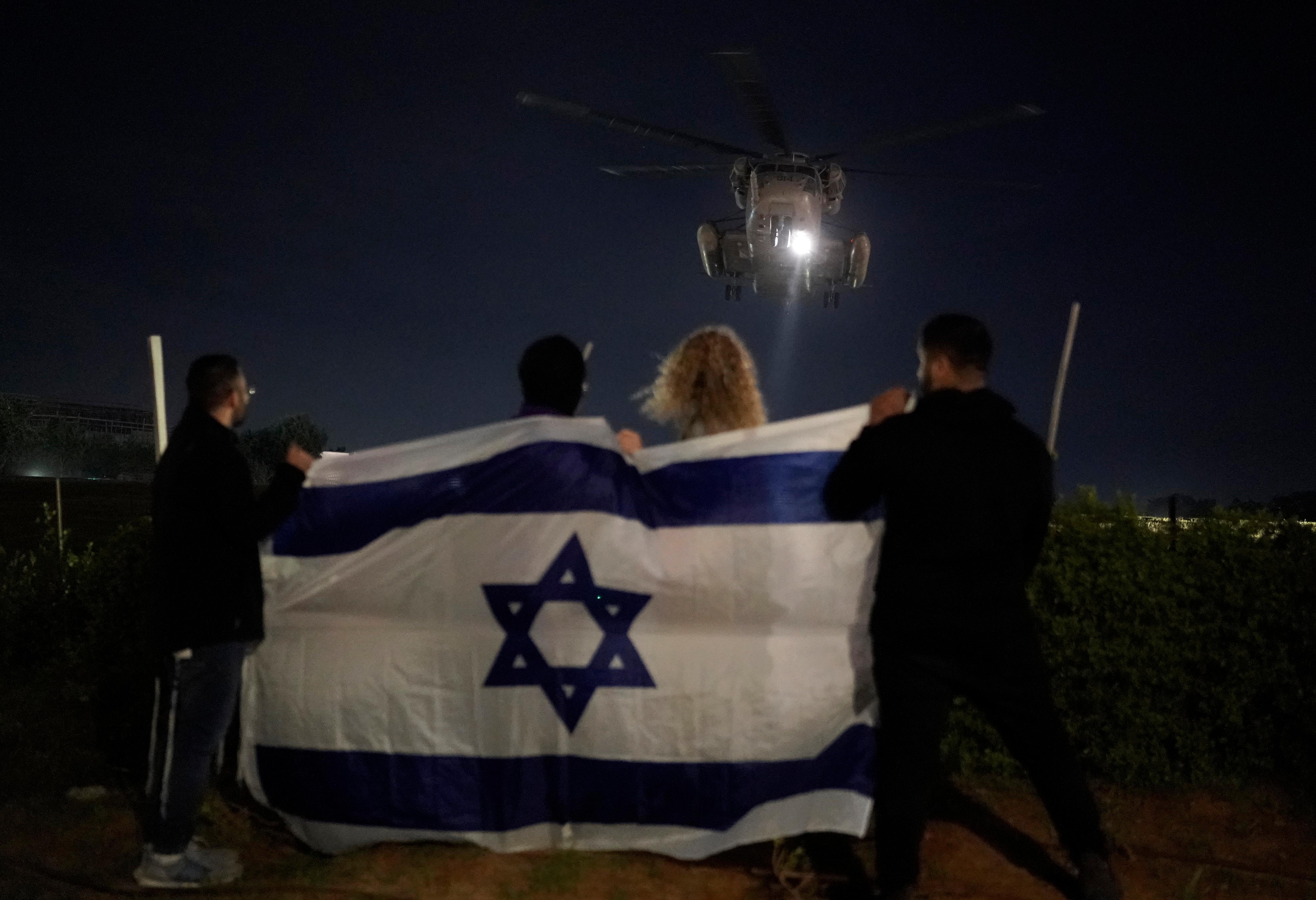 People holding an Israeli flag watch the arrival of a...