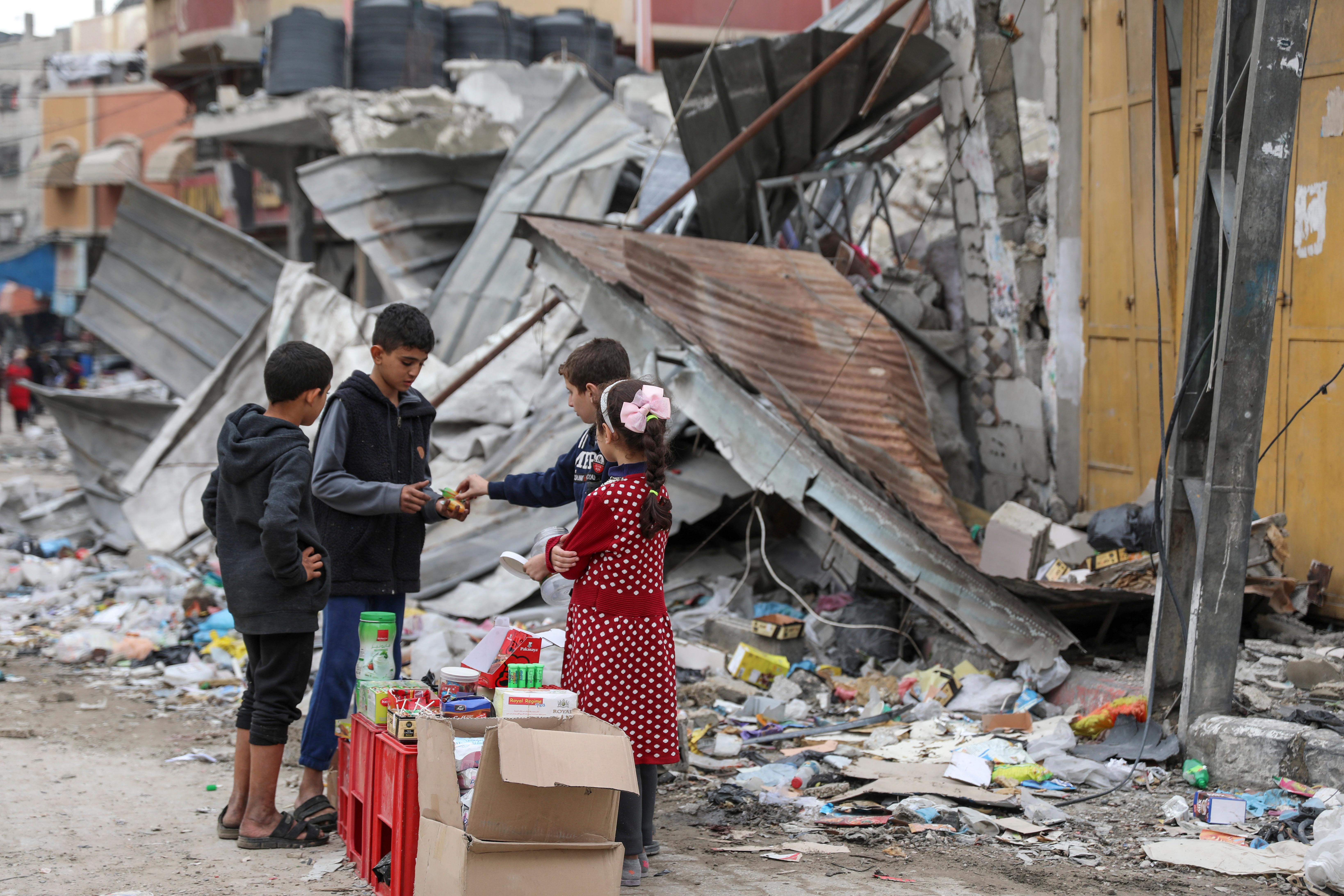 Palestinian children sell sweets in front of the rubble of...